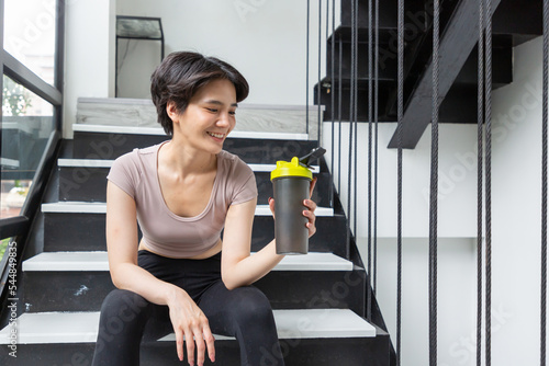 Athlete girll sitting in a black tight-fitting sports suit with a drinking bottle and sitting on the stairs. photo