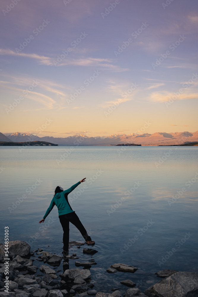 Woman balancing in the shore of lake at sunset. Mountainside landscape