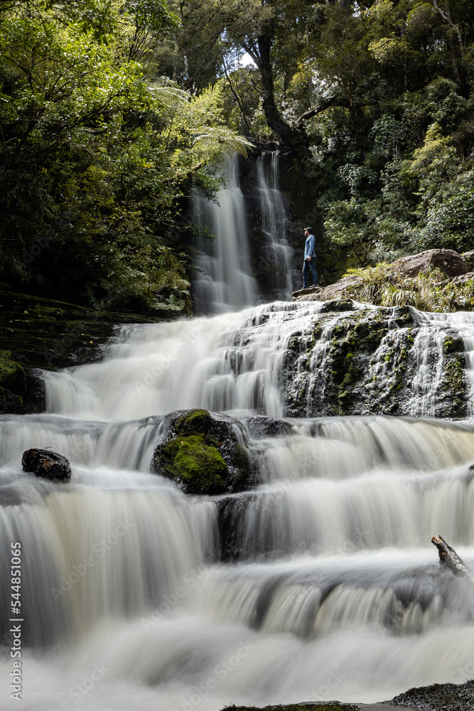 Obraz premium Man looking at the water flowing in waterfall in the middle of the rainforest