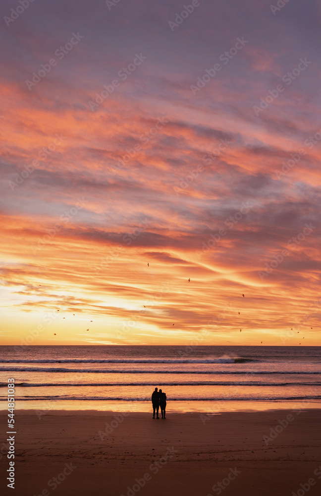 Couple silhouette embracing each other looking at dramatic sunrise at the beach.