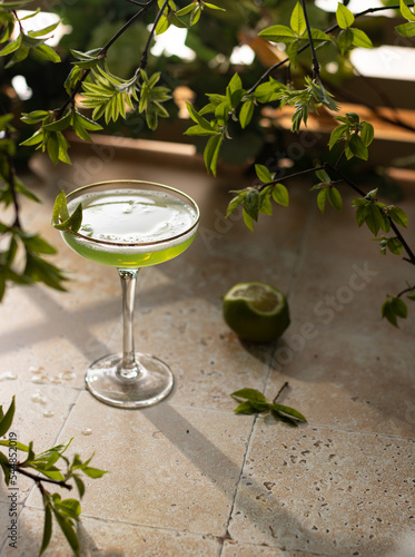 Beautiful green coctail with mint syrup,lime and green leaves on stone background.Close up of elegant drink in crystal glass.