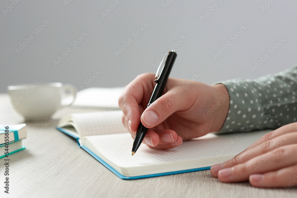 Woman writing in notebook at wooden table in office, closeup Woman writing in notebook at wooden table in office, closeup