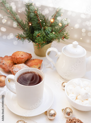  Winter, Christmas, New Year decoration composition, concept, background. White Mug, cup of hot tea, coffee, meringue, knitted plaid. Christmas lights. Christmas mood morning. Xmas greeting card.