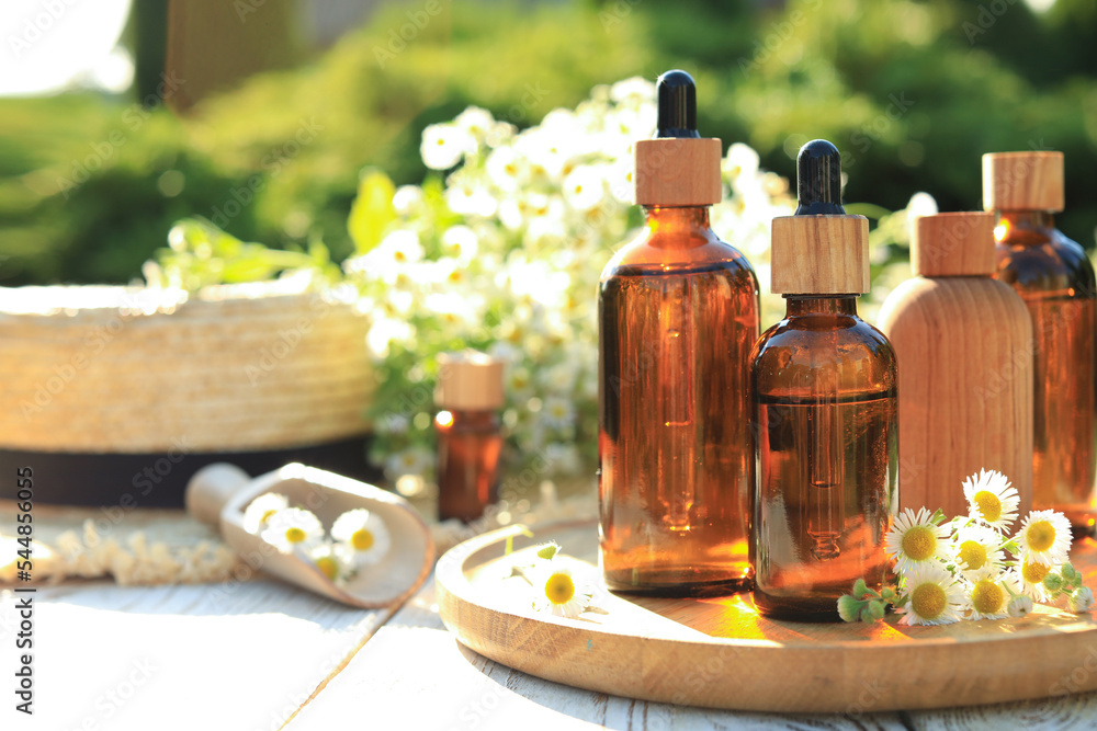Bottles of essential oil and flowers on white wooden table outdoors, space for text Bottles of essential oil and flowers on white wooden table outdoors, space for text