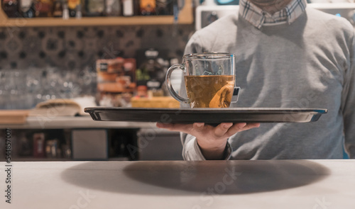 Camarero irreconocible, sirviendo té con bandeja, en la barra de una cafetería.