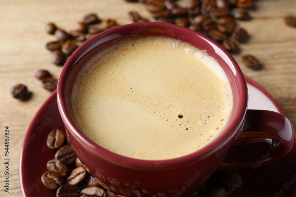 Cup of hot aromatic coffee and roasted beans on wooden table, closeup Cup of hot aromatic coffee and roasted beans on wooden table, closeup