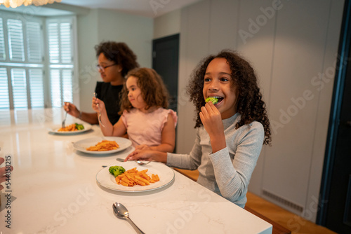Three smiling sisters enjoying dinner in kitchen