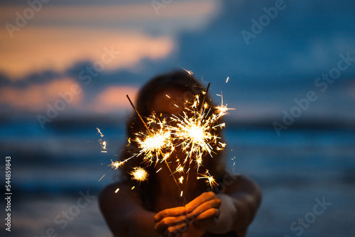 Obraz na plátně Woman with sparklers on the beach at sunset