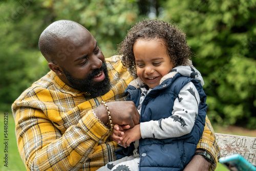 Smiling man with daughter on laps sitting on bench in park