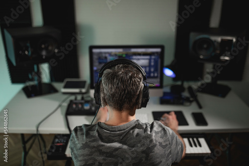 Music producer seen from behind listening with headphones to the project he is currently working on at his home studio