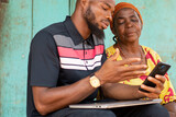 young black man showing an old african woman content on his phone