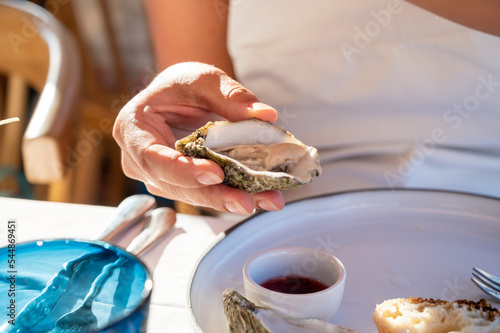 Young woman in white dress eats fresh live oysters with marinated onion, seafood in French restaurant photo