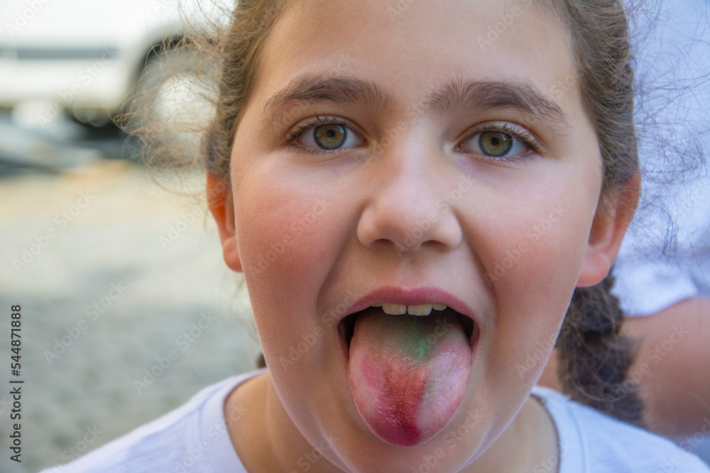 A teenage girl ate a candy and shows a colored tongue. The concept of