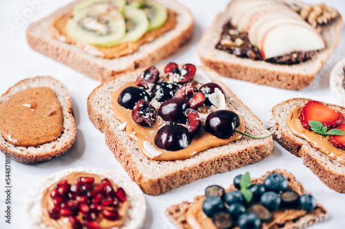 Various kind of open sandwiches with berries and fruits. Made from bread, such as wholegrain, rice crakers, crispbreads and different nut butter, such as peanut, crunchy cashew and almond butter