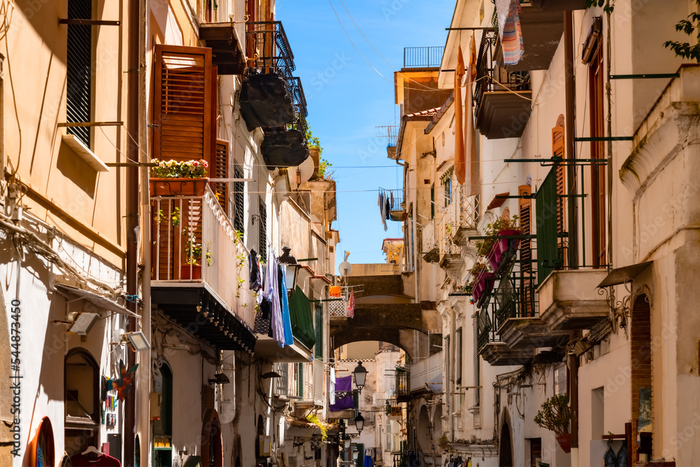 Narrow road “Via Pietro Capuano“ and main street in the old town of Amalfi city in Italy. World heritage destination and popular tourist destination with old facades with balconies, shops and cafes.