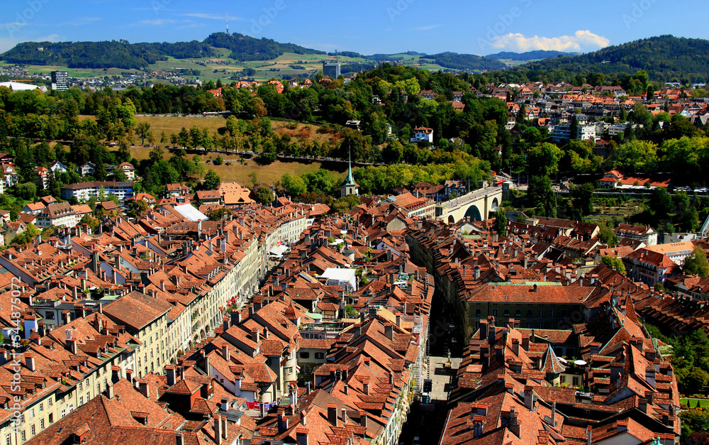 Panorama of the historic part of Bern with red-roofed houses, winding streets and arched bridge with mountains in the background