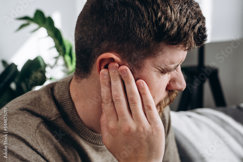 Fényképezés Close-up of unhealthy young caucasian man 30s touching ear, suffering from sudden throbbing ear ache, looking aside