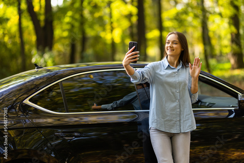 Selfie time. Portrait of young woman standing on background of white car and doing selfie. photo