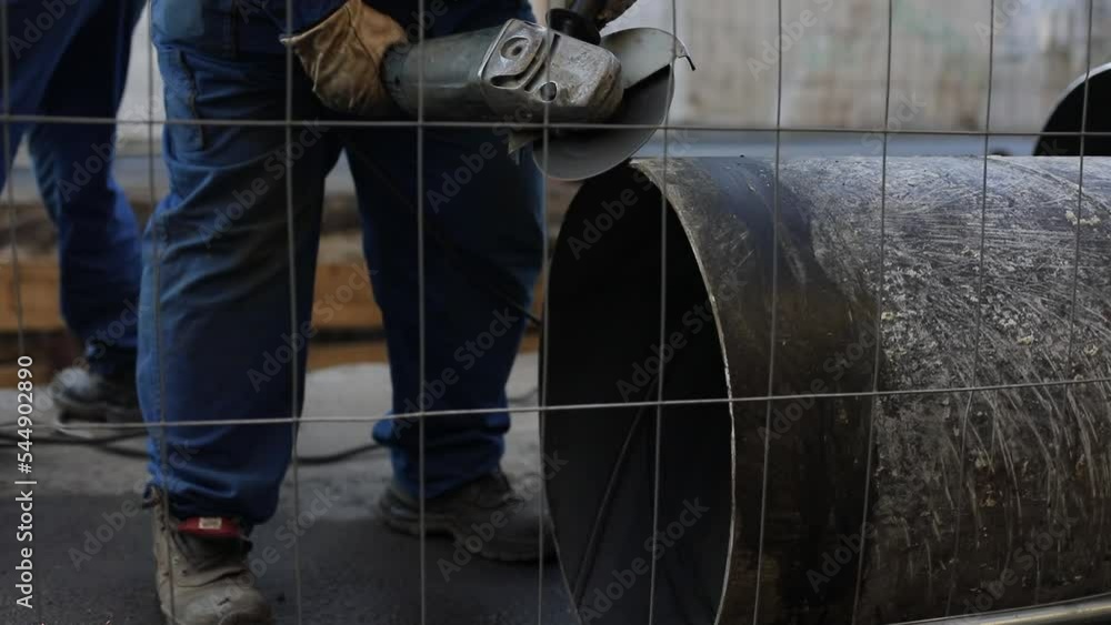 Details with a worker using an angle grinder on an industrial metallic pipeline. Details with a worker using an angle grinder on an industrial metallic pipeline.