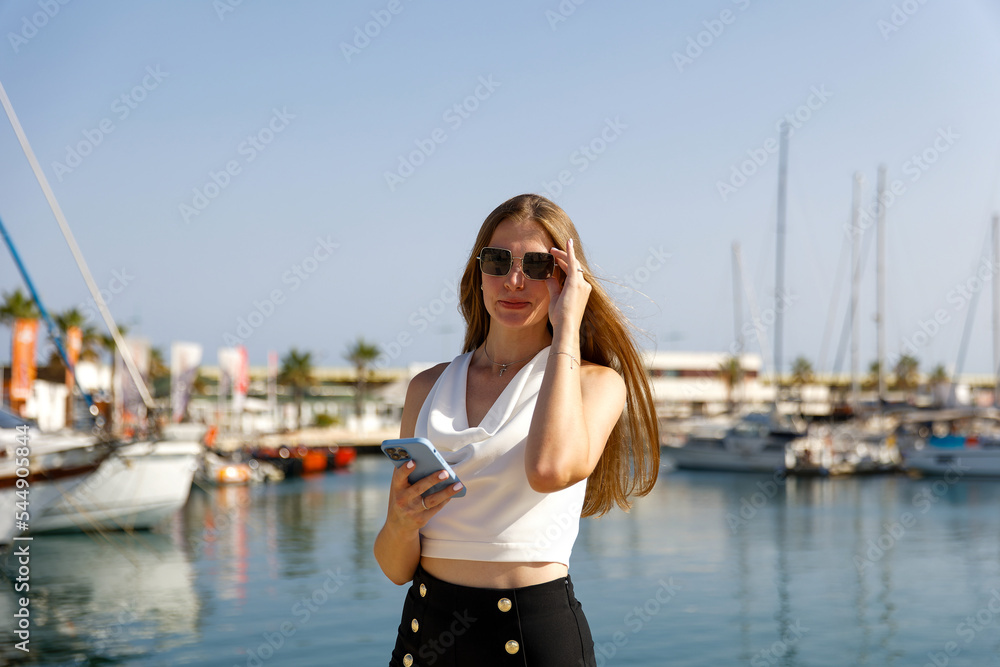 Beautiful woman in talking on the phone against the backdrop of the blue sea and yachts