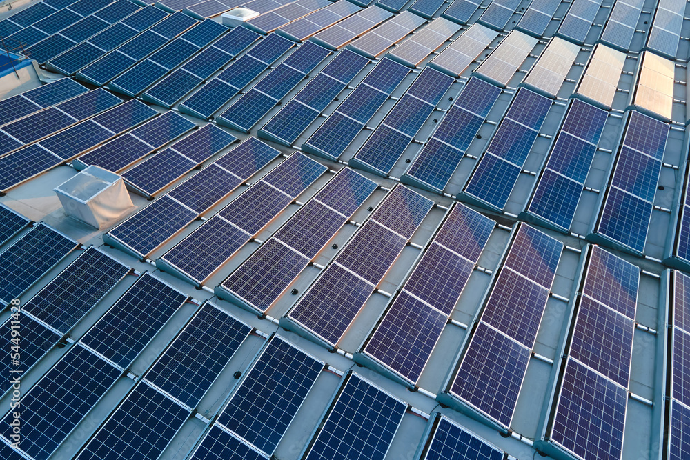 Aerial view of blue photovoltaic solar panels mounted on industrial building roof for producing green ecological electricity. Production of sustainable energy concept Aerial view of blue photovoltaic solar panels mounted on industrial building roof for producing green ecological electricity. Production of sustainable energy concept