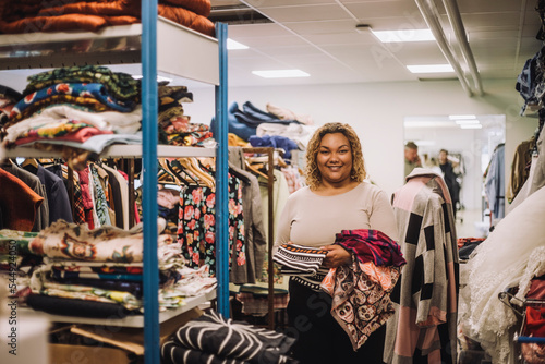 Portrait of smiling female fashion designer holding fabrics while standing at workshop photo