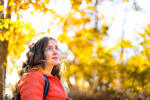 Young woman face portrait with blue eyes on hiking trail colorful yellow orange foliage fall autumn forest bokeh background on cold sunny day in Great Falls, Virginia and Maryland