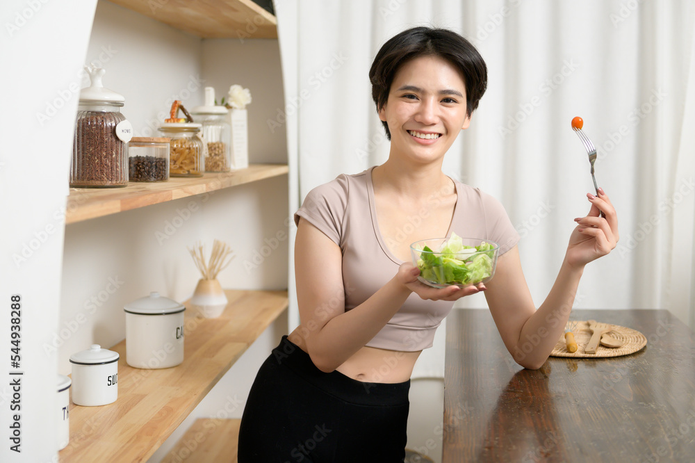 An Asian young woman in sportswear eating vegetables salad in kitchen at home , healthy lifestyle concept An Asian young woman in sportswear eating vegetables salad in kitchen at home , healthy lifestyle concept