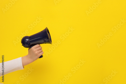 children's hand holding a megaphone on a yellow background with copy space