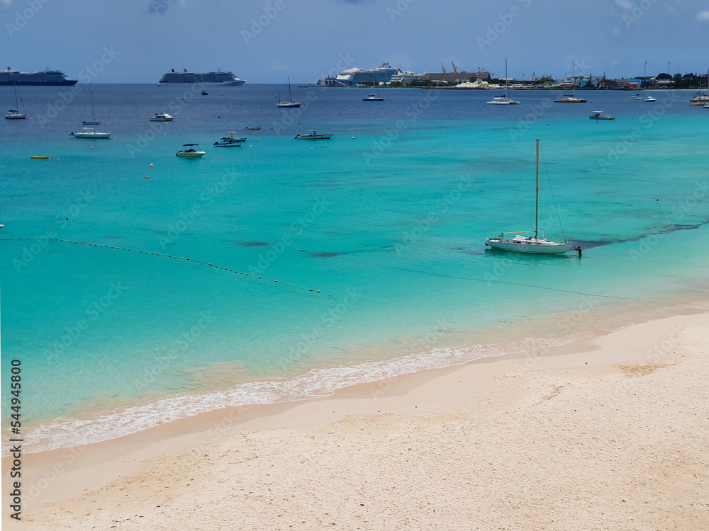 beautiful tropical beach with blue turquoise water in the ocean, Barbados. View on port, ships, vessels, cruises and fishing boats in harbor. Wave meet sand  