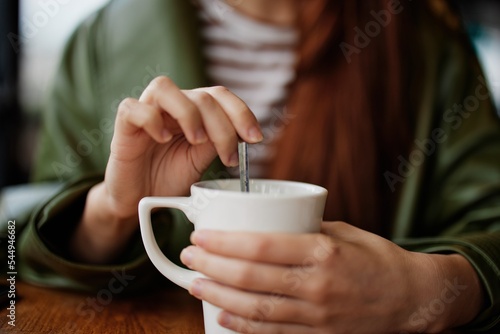 Woman in cafe stirring sugar in white coffee mug, autumn vibe and warmth