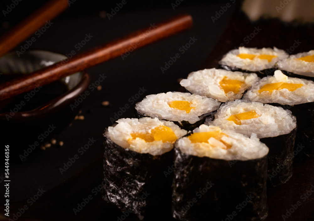 Cheese and mango maki, Japanese sushi, delicious Japanese food with black background and decorated with chopsticks and a bowl of soy sauce, for oriental and Asian food restaurant. Cheese and mango maki, Japanese sushi, delicious Japanese food with black background and decorated with chopsticks and a bowl of soy sauce, for oriental and Asian food restaurant.