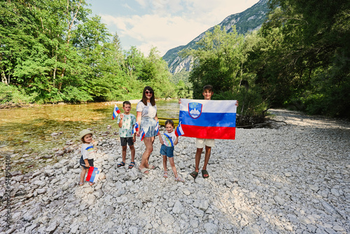 Photos Mother with kids hold slovenian flags in rocky shore of a calm river in Triglav National Park, Slovenia
