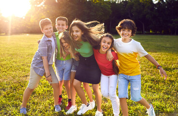 Group of happy cheerful active little children enjoying summer break, meeting in park, frolicking on green grass, playing fun games, making new friends, hugging, smiling and having great time together