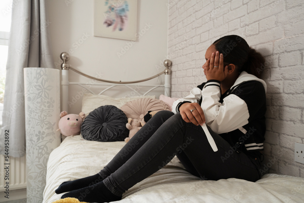 Girl sitting on bed with pregnancy test - obrazy, fototapety, plakaty 
