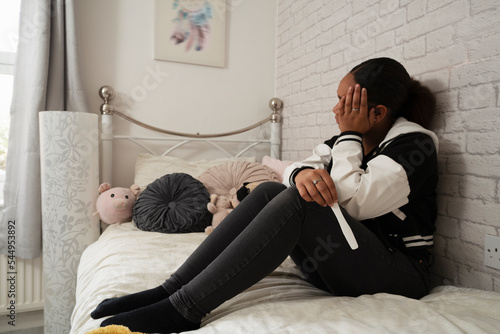 Girl sitting on bed with pregnancy test