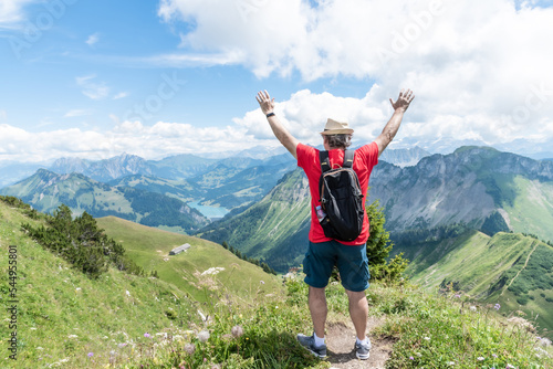 Senior adult man with hat, backpack and red shirt with his arms up looking towards the Swiss Alps.