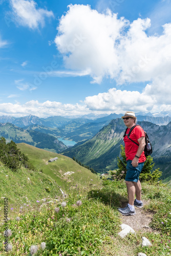 Vertical photo of senior adult man with sunglasses, cap and backpack on mountain with the Swiss Alps