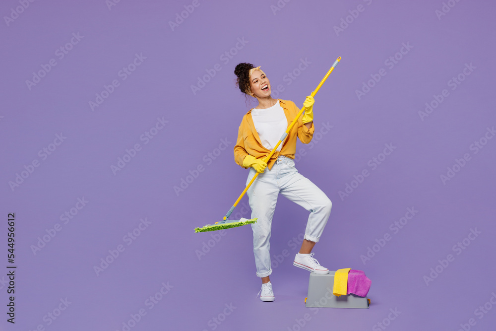 Full body side view happy young housekeeper woman wear yellow shirt tidy up hold mop bucket with water wash floor look aside isolated on plain pastel light purple background studio. Housework concept.