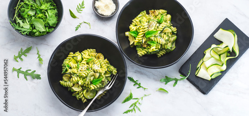 Green vegetarian fusilli pasta with zucchini pesto and herbs on a white marble background in a black bowl. Healthy and economical recipes for the whole family, Italian pasta, internet banner
