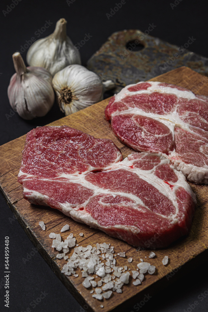 A slice of raw fresh meat on a wooden board on a black background.