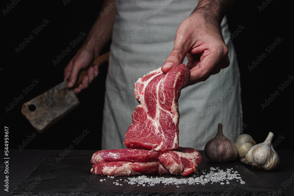 The hand of the cook holds a slice of raw fresh meat on a black background.