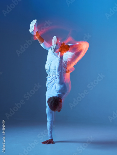 Fototapeta Naklejka Na Ścianę i Meble -  Portrait of professional male athlete, sportsman training in studio, upside down stands on one hand on blue background.