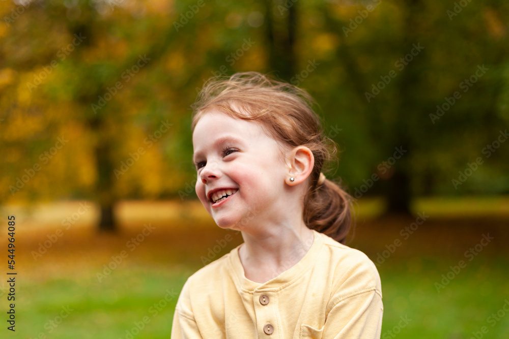 Lovely cute red-haired little girl in the autumn park outdoors. Lovely baby in front of falling leaves