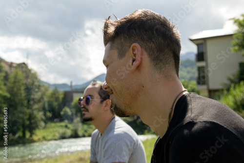 Stock image of two male friends sitting by the river and chilling, relaxing on a sunny day.
