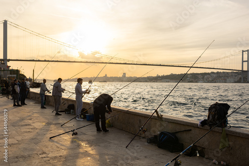 Fishermen on sunset. Istanbul bosporus at background. Silhouette photo. Unrecognizable people.