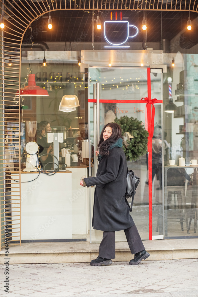 Young woman in black coat walking in city. Facade of cozy cafe.