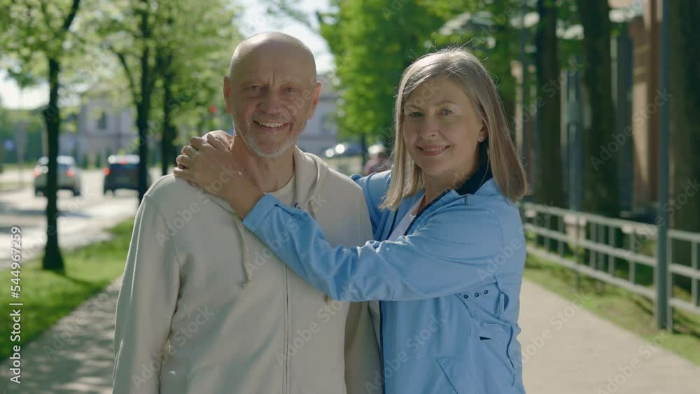 Happy matured couple wearing sportswear while embracing each other on the street background. Portrait elder joggers family looking at camera. Sport and healthy lifestyle concept. Aging Youthfully Happy matured couple wearing sportswear while embracing each other on the street background. Portrait elder joggers family looking at camera. Sport and healthy lifestyle concept. Aging Youthfully