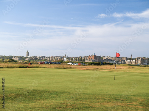 Red hole flag on golf course with urban skyline behind