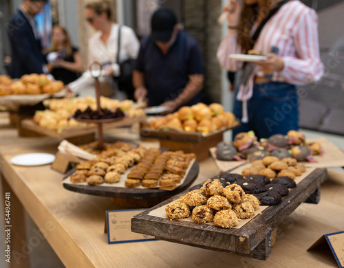 Snack bar counter at an event. Assorted selection of desserts and local delicacies. People select food what they want to eat. Unrecognizable people.